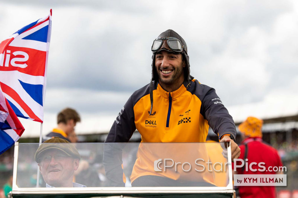 Daniel ricciardo tersenyum dan mengendarai mobil convertible di depan silverstone grand pric