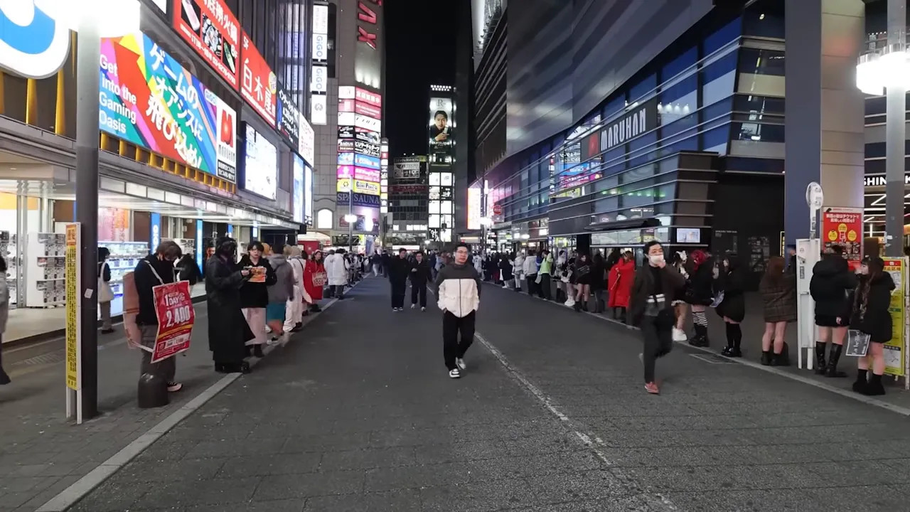 Crowded Shinjuku street at night with neon signs and shoppers moving along the sidewalk