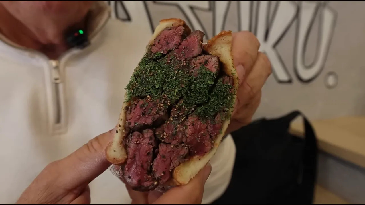 Hand holding a wagyu sandwich with herb seasoning close to the camera