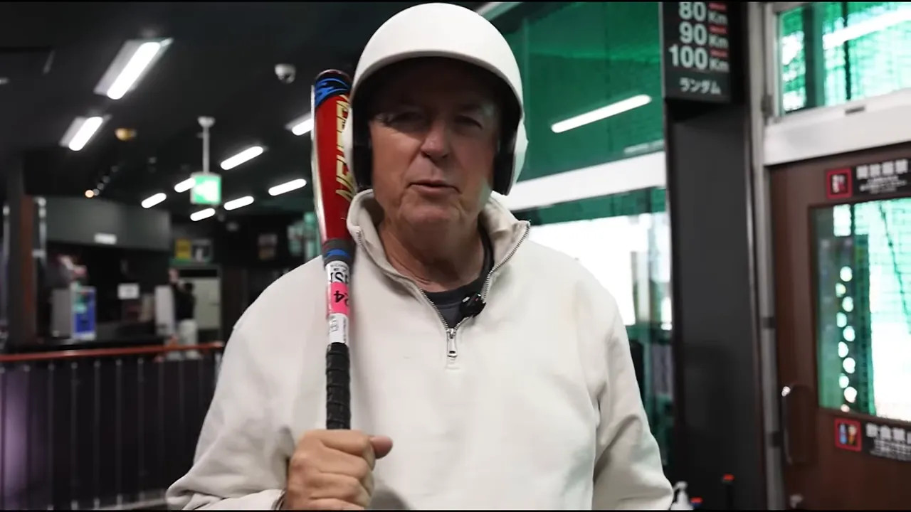 Person in a Tokyo batting cage holding a bat with a helmet and headphones