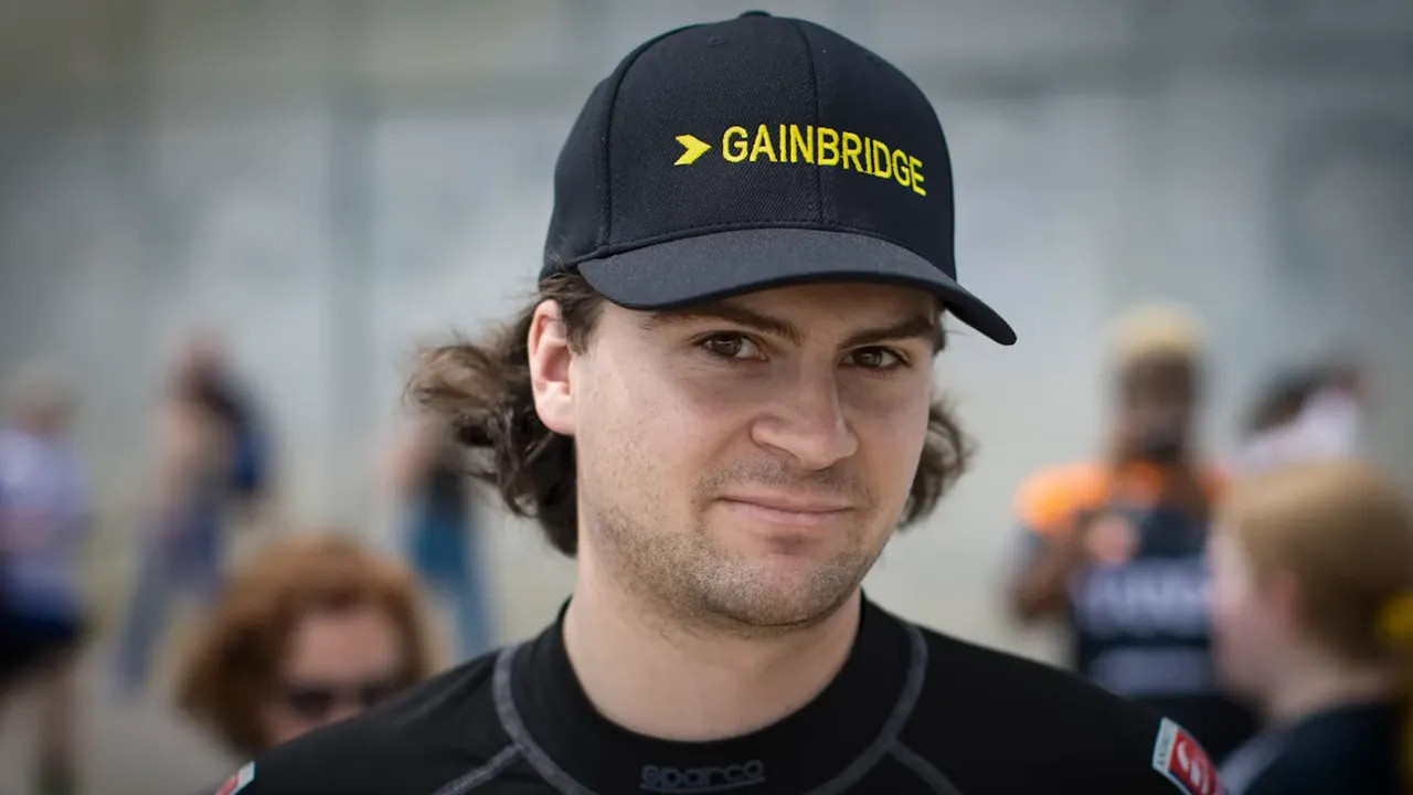 Close-up of a feeder-series driver wearing a black cap with visible sponsor branding, photographed at a paddock event.