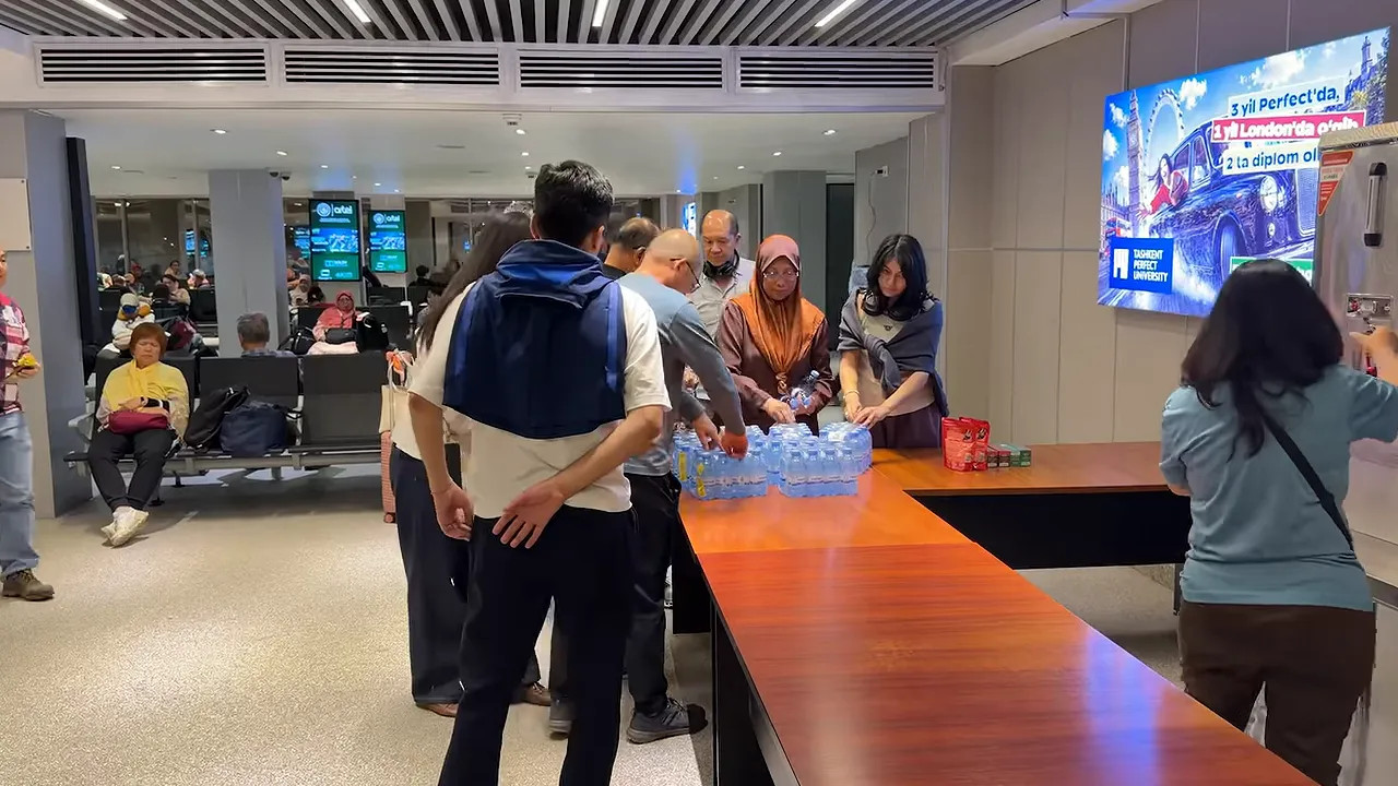 Passengers collecting bottled water from a table in an airport holding area
