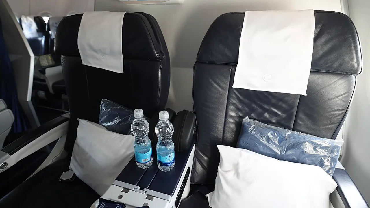 Two black business class seats with pillows, wrapped blankets and water bottles