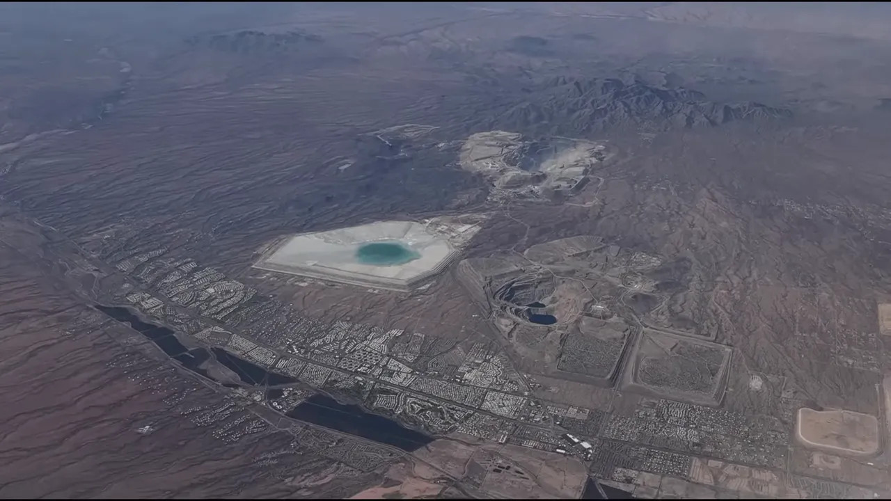 Clear aerial photograph of desert terrain with a hexagonal turquoise pond and adjacent urban areas, taken from the aircraft during approach