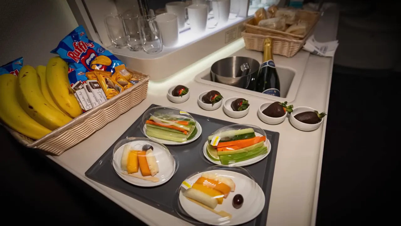 In‑flight self‑serve snack spread with plated vegetable sticks, cheese, chocolate‑covered strawberries, bananas, chips and a bottle of champagne