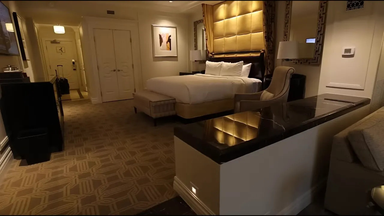 Wide hotel suite view showing a lounge area, marble divider, king bed and seating