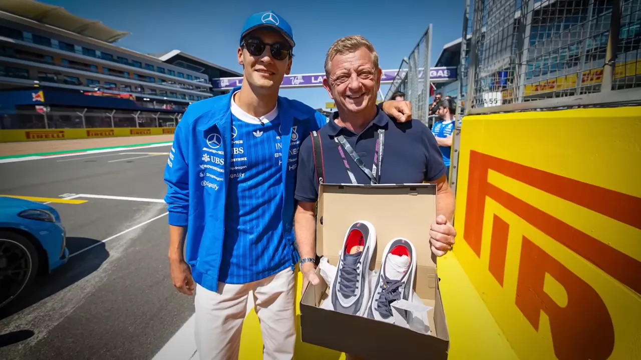 George Russell and a smiling man posing with an open shoe box containing signed trainers
