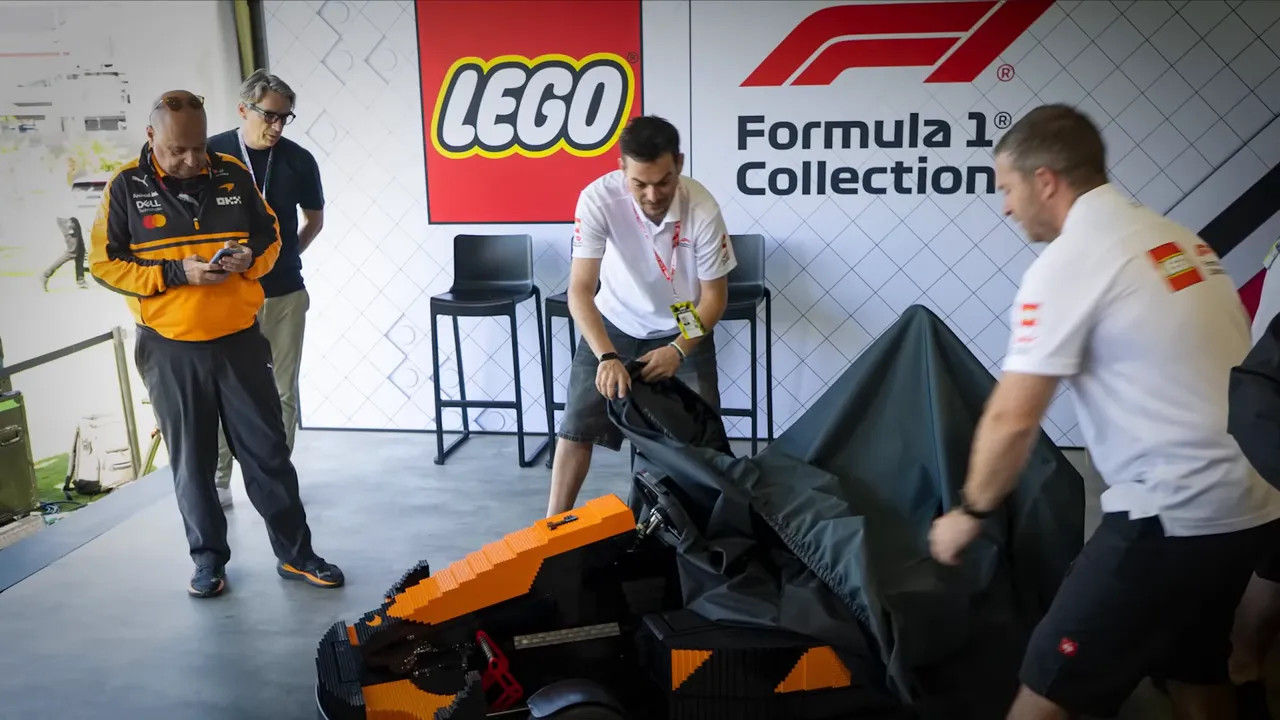 LEGO and Formula 1 Collection signs behind staff uncovering an orange LEGO car
