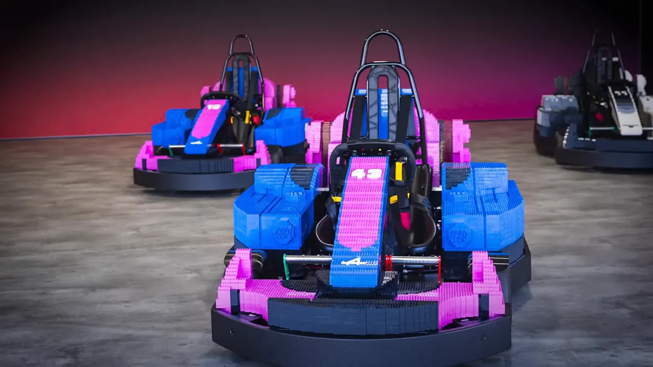 Pink and blue LEGO Formula 1 style go karts displayed on a floor against a dark backdrop