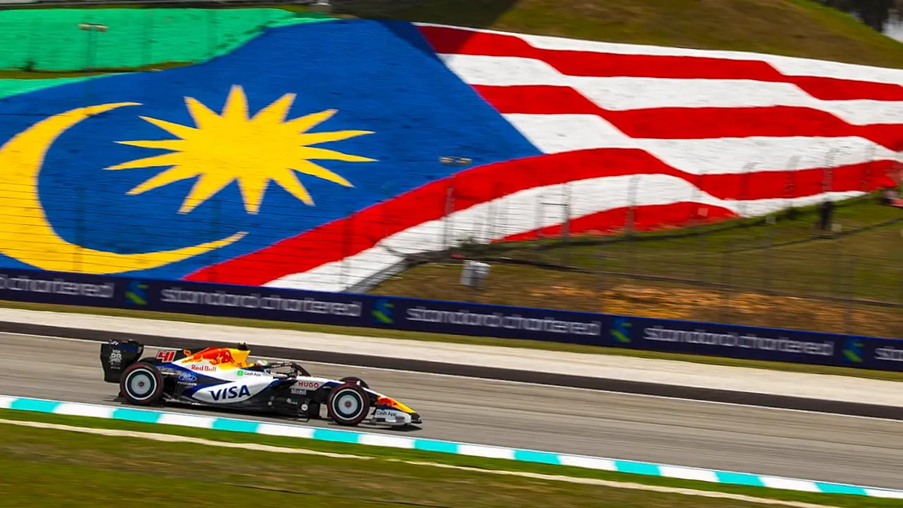 Formula 1 car passing beneath a huge Malaysian flag displayed on the hillside