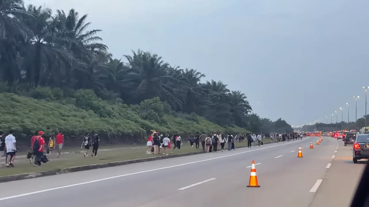Groups of pedestrians walking beside a road with motorcycles, cars and traffic cones