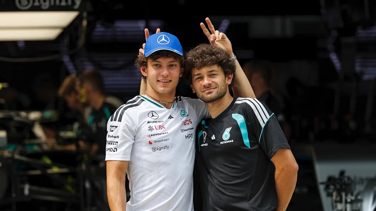 Mercedes driver posing beside his photographer, who holds two fingers above the driver's cap
