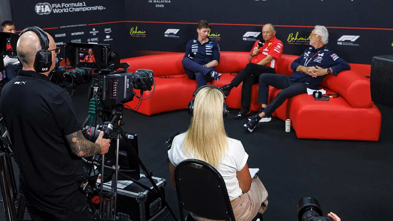 Press conference room with an interviewer facing guests seated on red sofas and a television camera