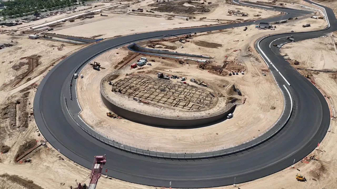 aerial view of a new circuit section with dark asphalt looping through sandy construction site