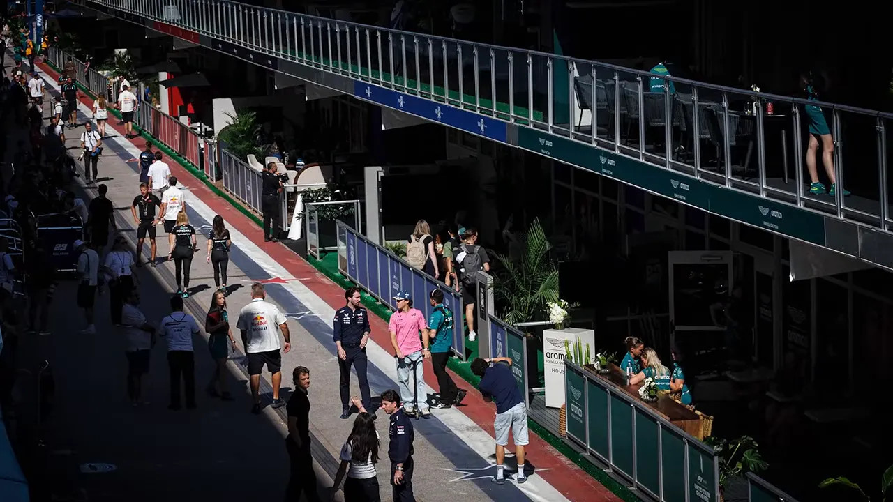 People walking through a narrow paddock lane beside team hospitality buildings