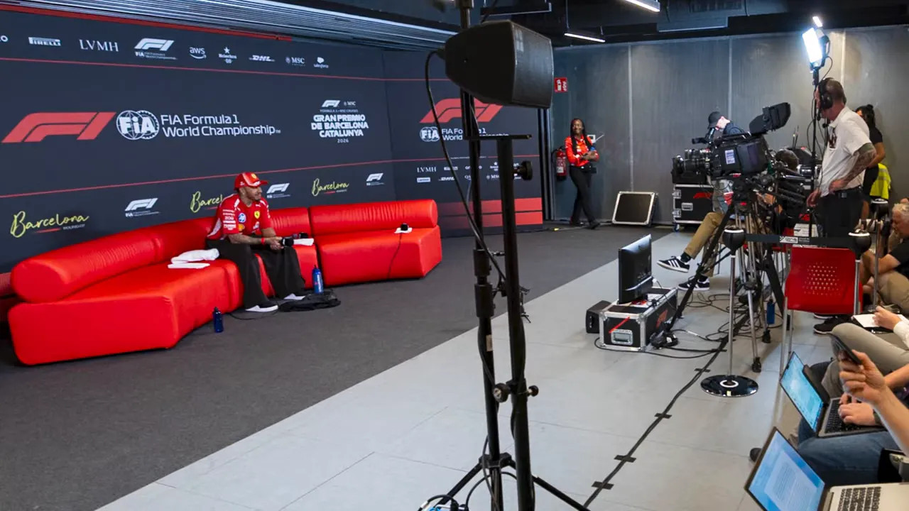 Press conference room with drivers on red couches and photographers in front