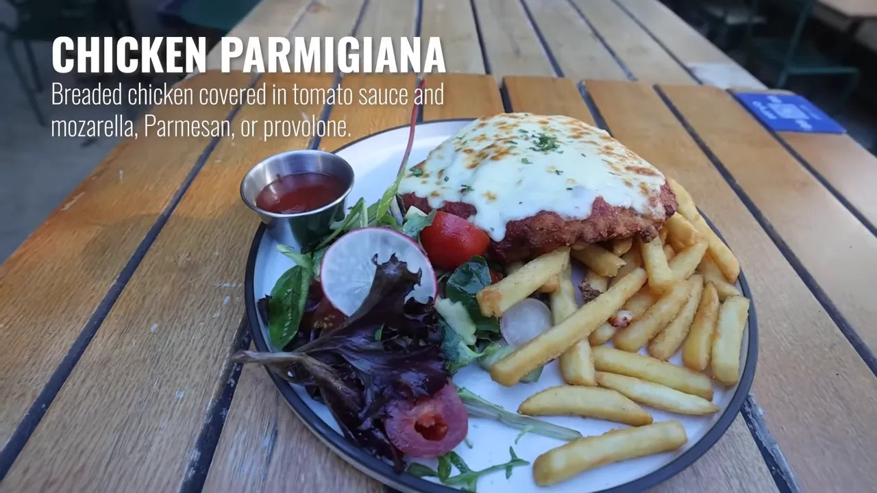 Chicken parmigiana (chicken parmi) served with tomato sauce, melted cheese, and chips