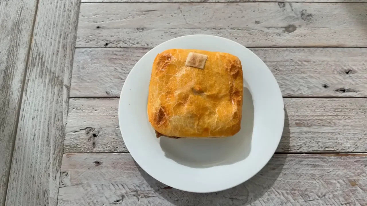 Single baked meat pie on a white plate on a wooden surface