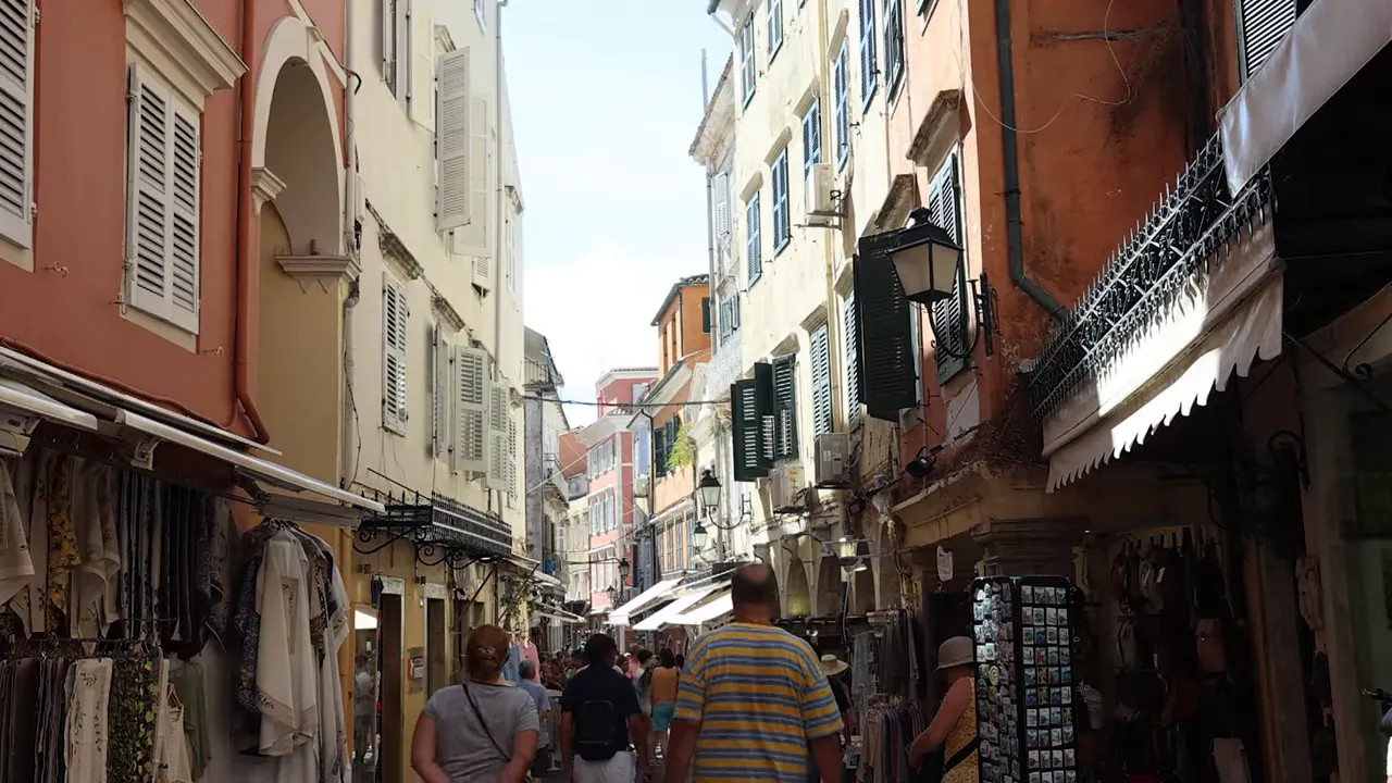 Narrow Corfu shopping street lined with tall buildings, shopfronts and pedestrians