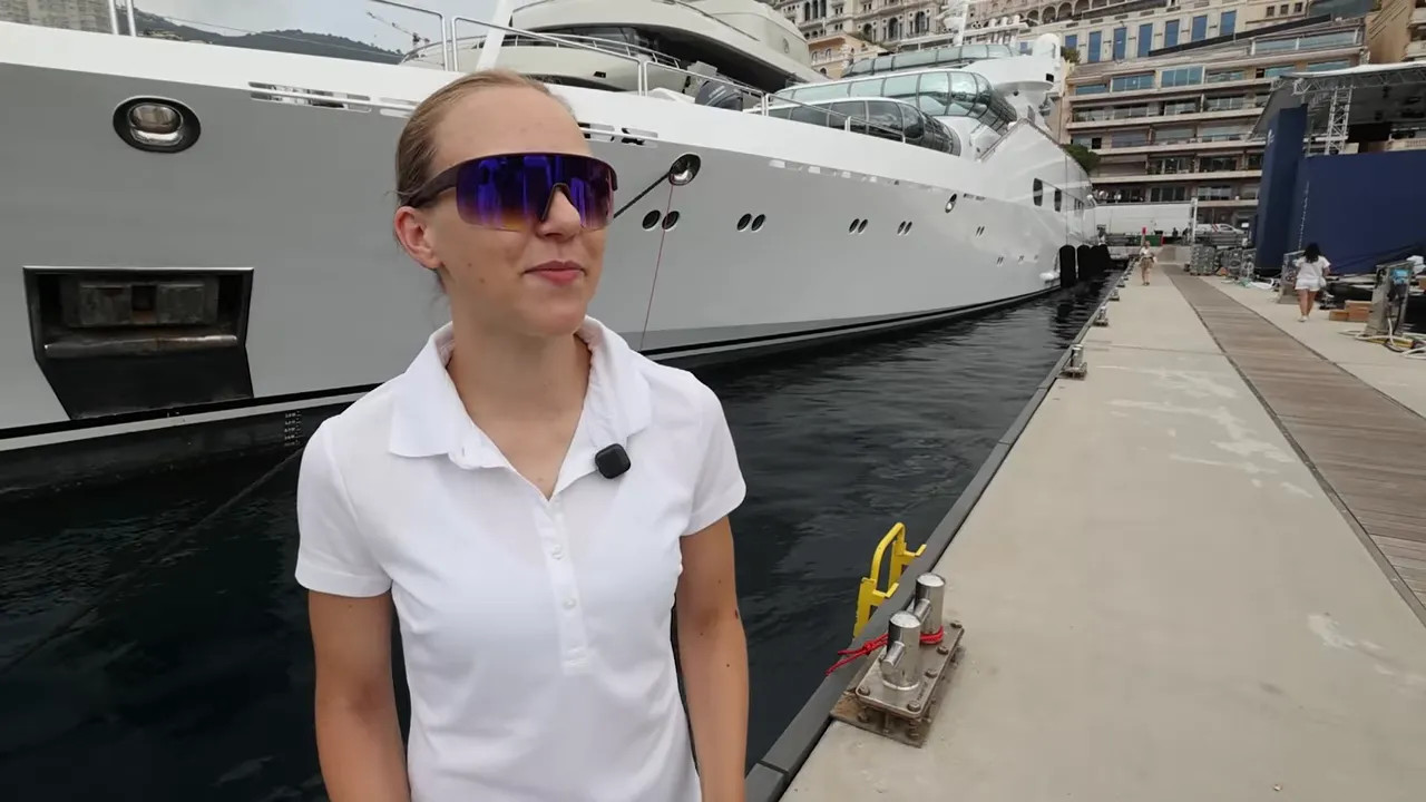 Woman in white polo and sunglasses holding papers on a marina dock beside yachts