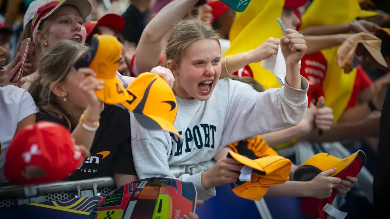 Female Formula 1 fans cheering with team flags and branded scarves in a packed grandstand