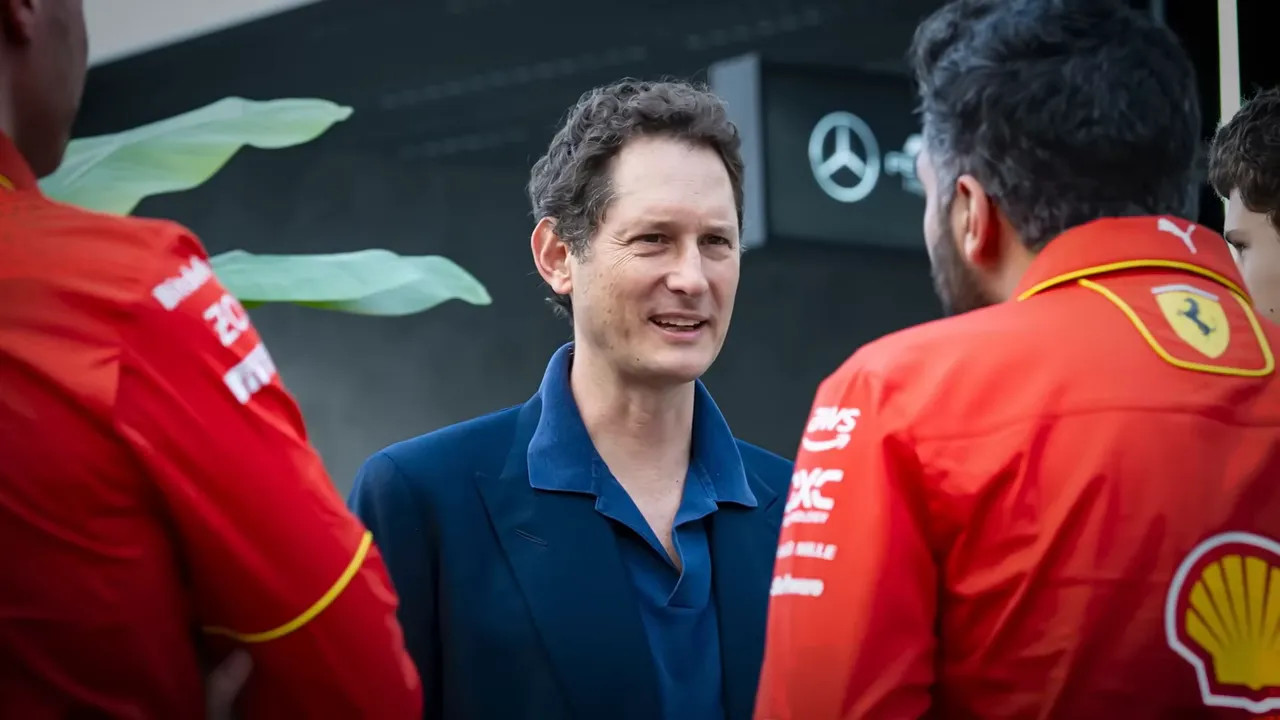A suited leadership figure speaking with Ferrari team members in the paddock