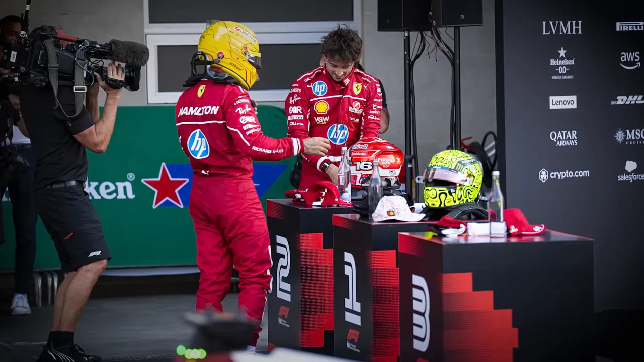 Drivers in Ferrari race suits at a podium being filmed by a cameraman during a media moment.