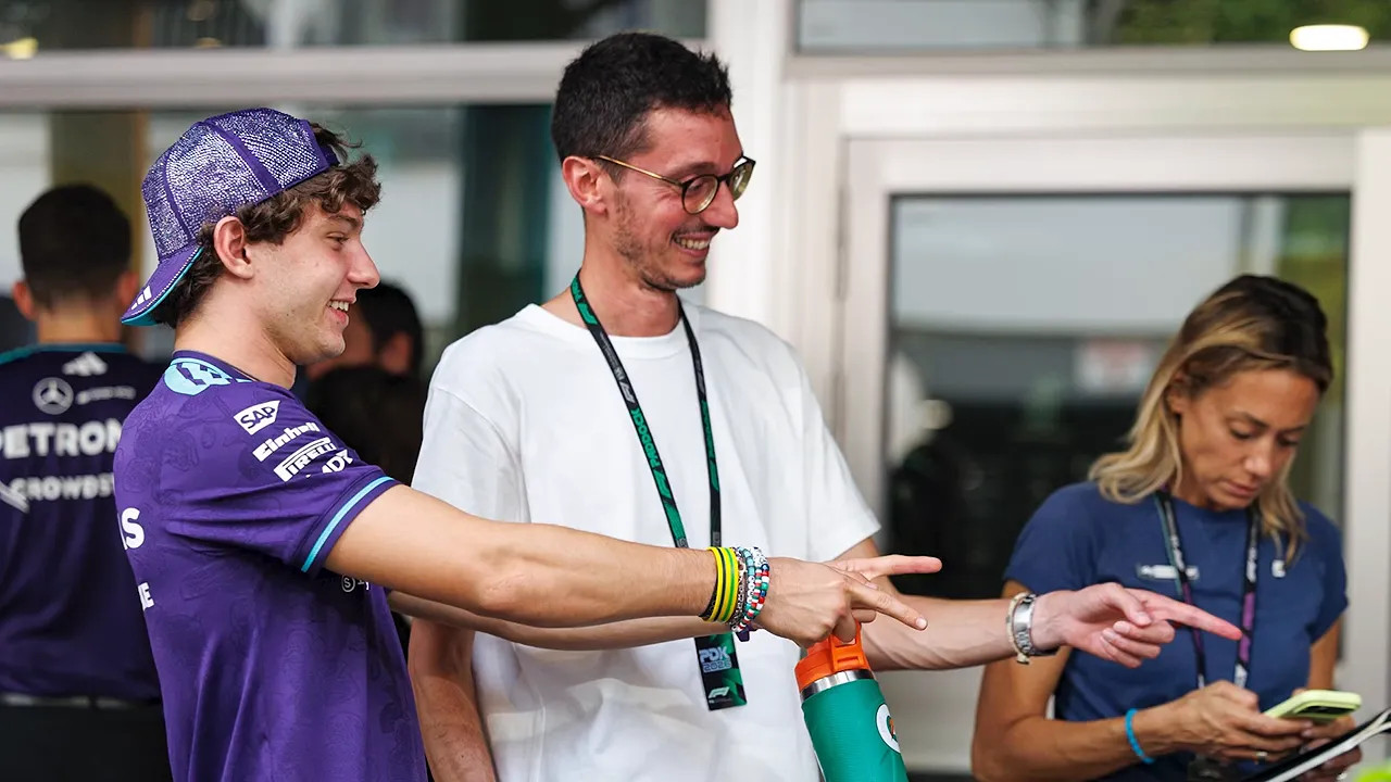Kimi Antonelli smiling and pointing beside a man wearing glasses and a credential