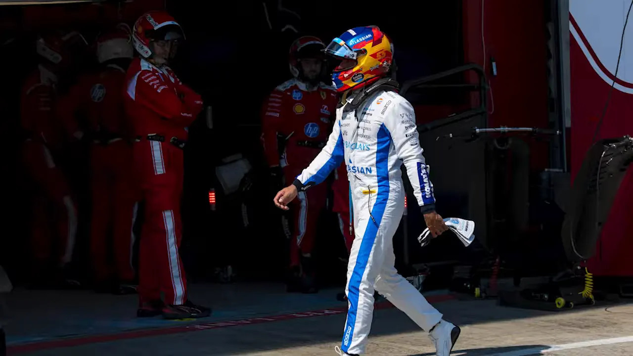 Carlos Sainz in white racing suit and helmet walking past the Ferrari garage area