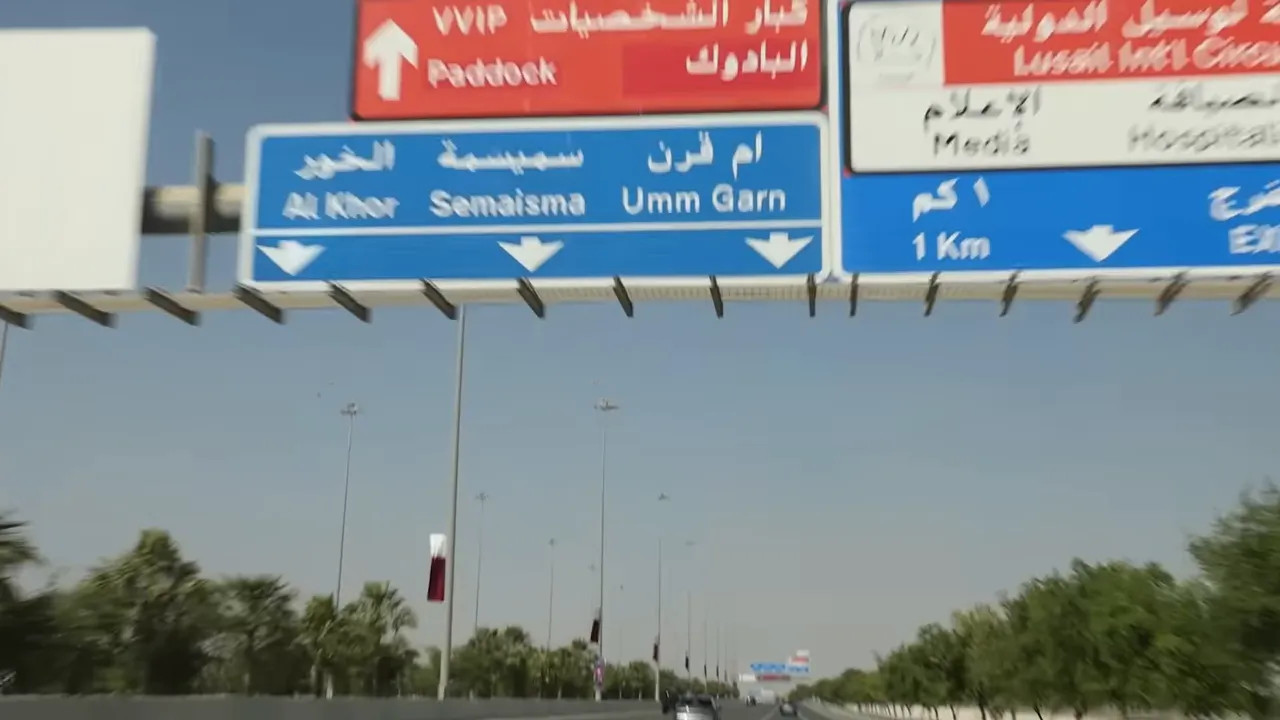 Highway overhead road signs in Arabic and English directing traffic to Paddock and Lusail