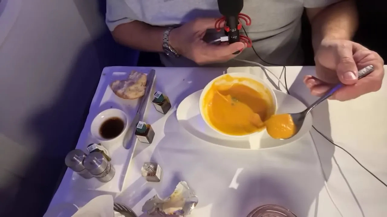 In-flight Qsuite meal with microphone and spoon showing a live-stream setup