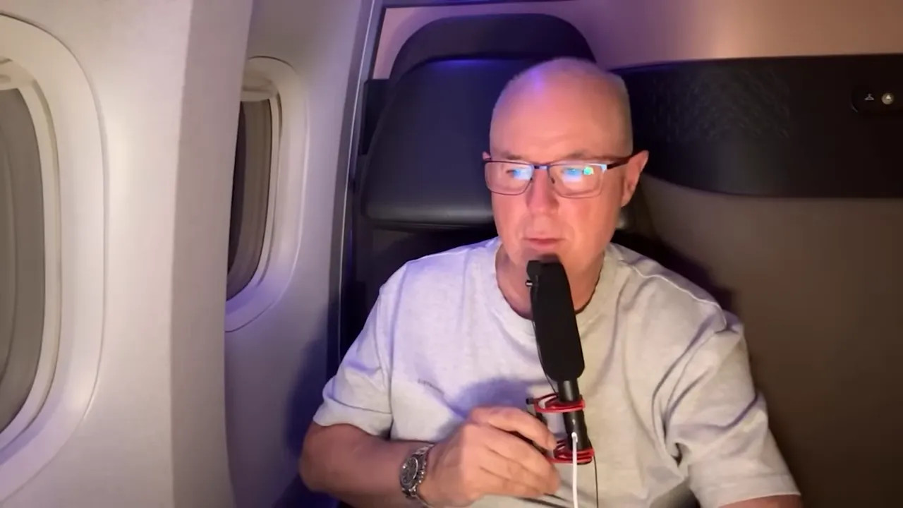 man live streaming from an airplane Qsuite with a microphone and window visible
