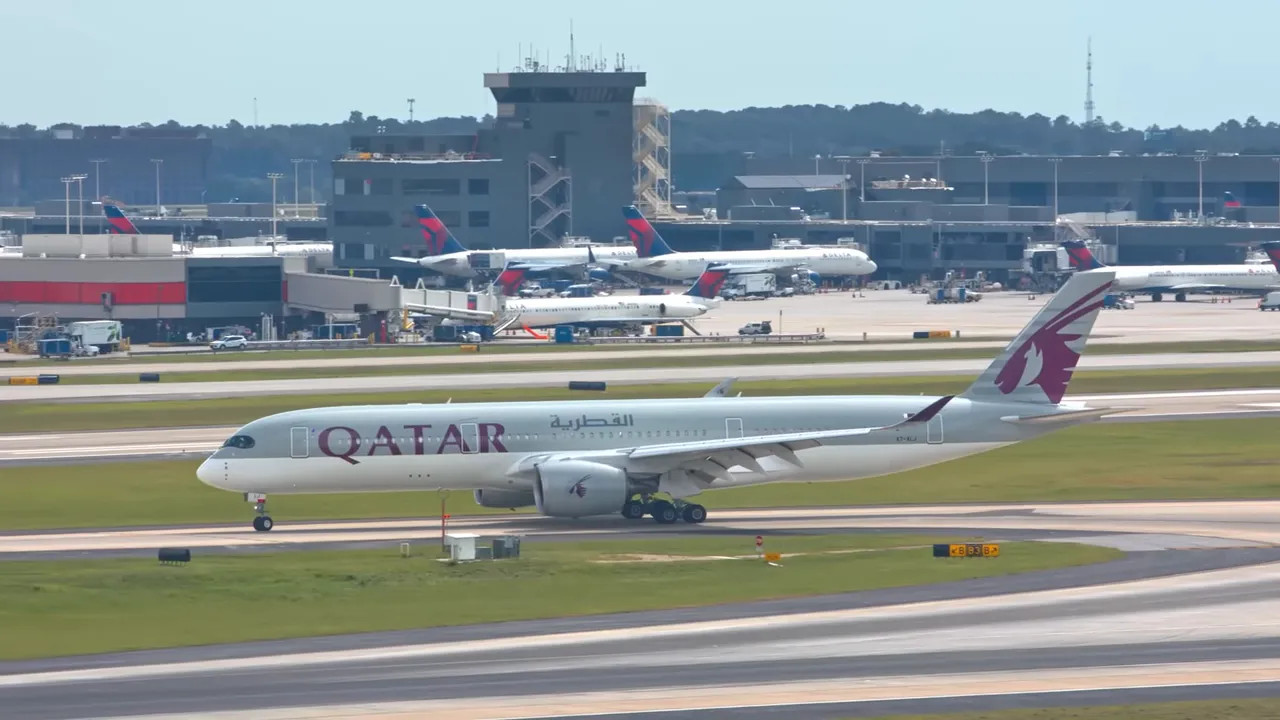 Qatar Airways aircraft taxiing at an airport with terminal buildings in the background
