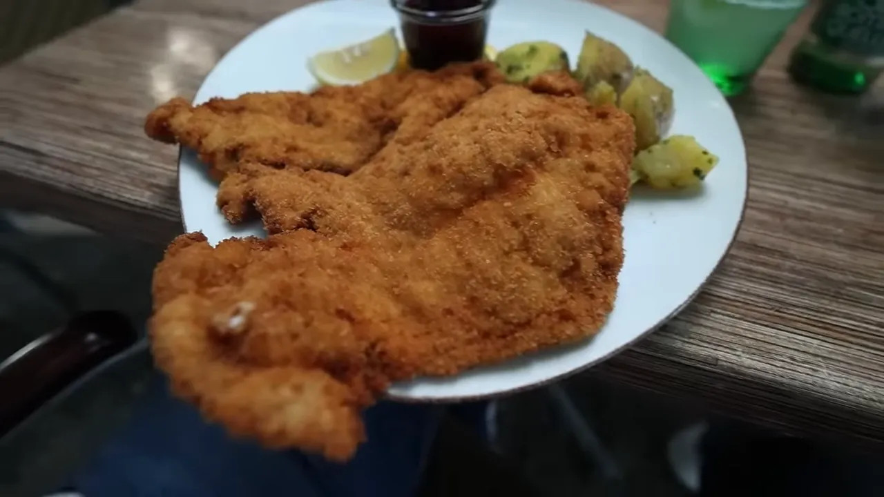 Large breaded schnitzel with potatoes lemon and a small cup of sauce