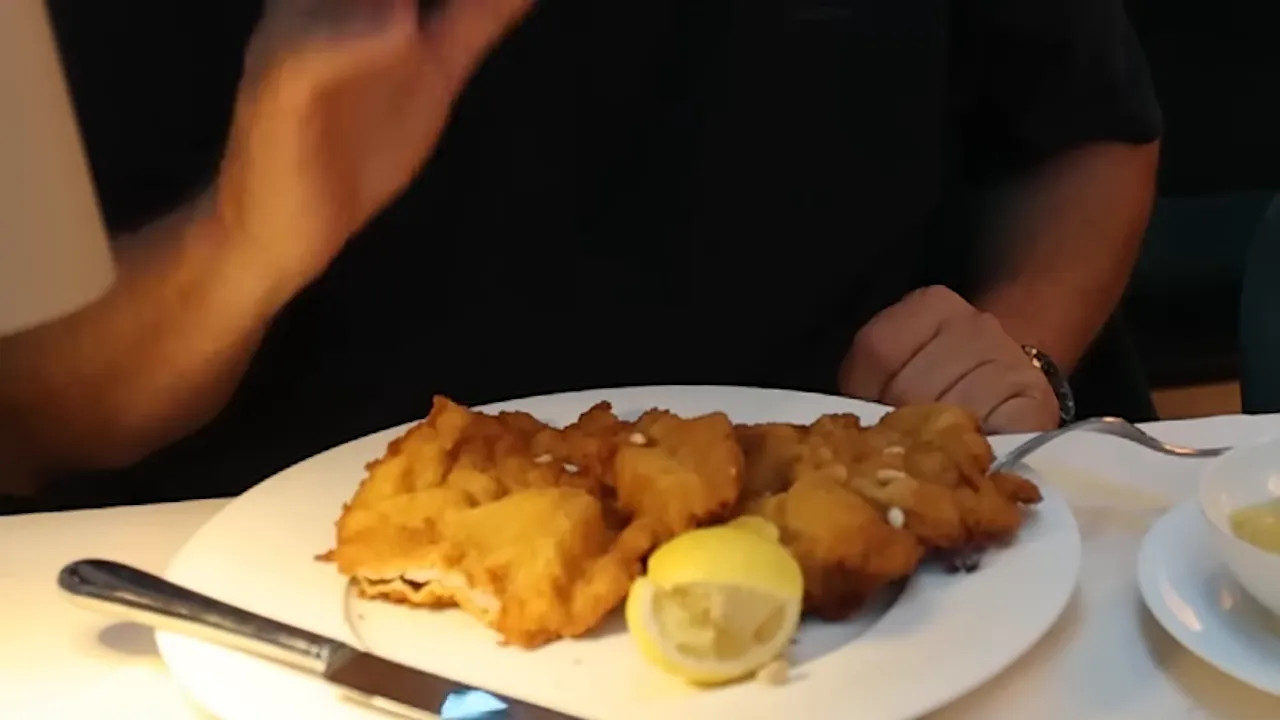 Two pieces of golden schnitzel with lemon wedges on a white plate
