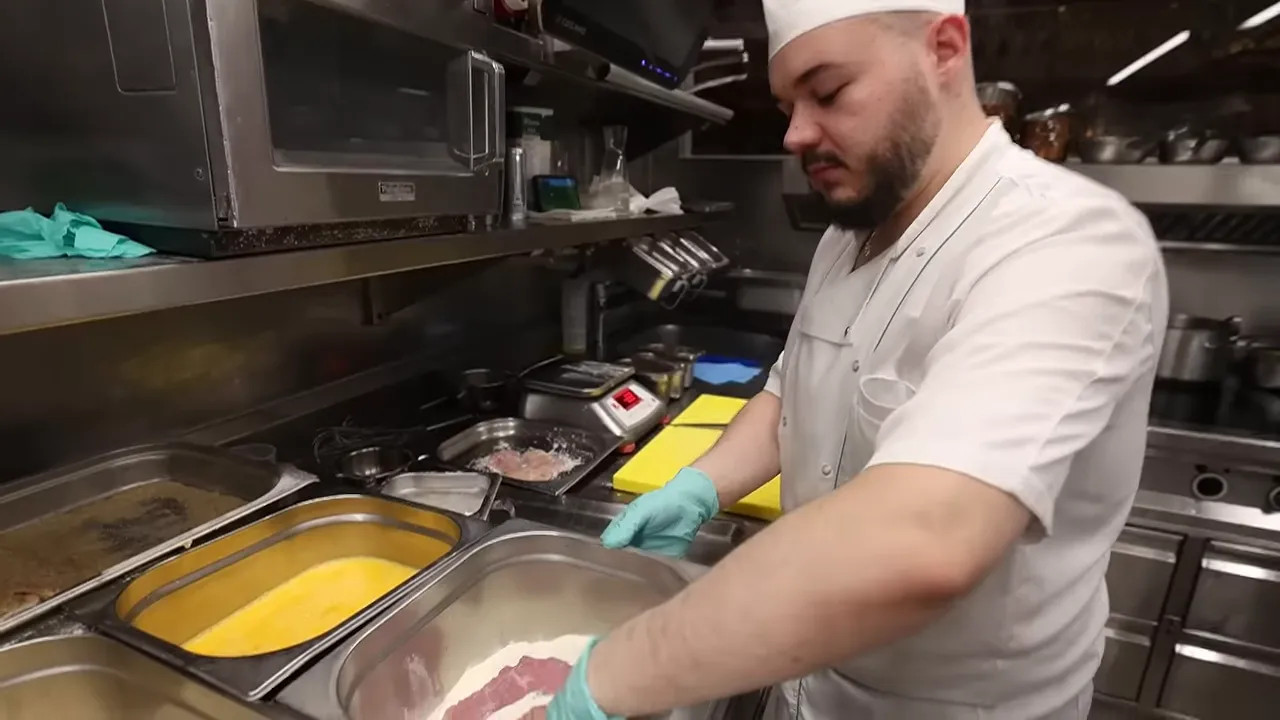 Veal schnitzel being dipped in egg and breadcrumbs in a kitchen