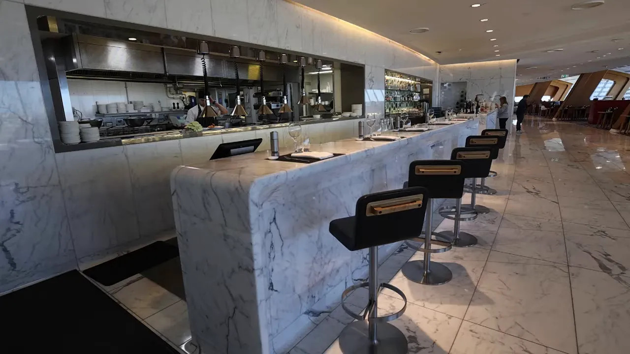 Marble bar seating with open kitchen pass and plated settings in a premium airline lounge