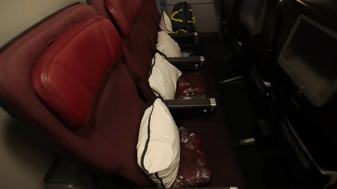 Three economy seats on Qantas A380 with pillows and plastic-wrapped blankets, seatback screens visible