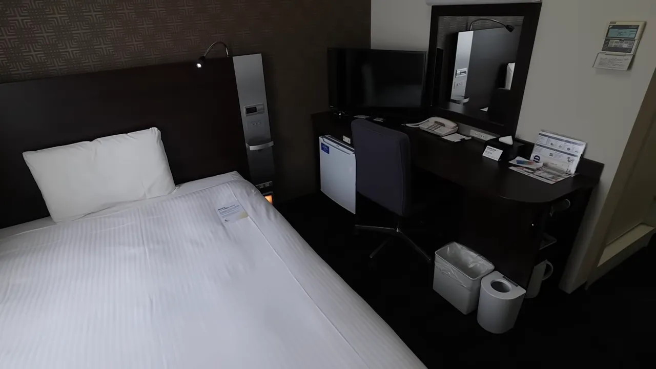 Small hotel room with bed, desk, and limited amenities
