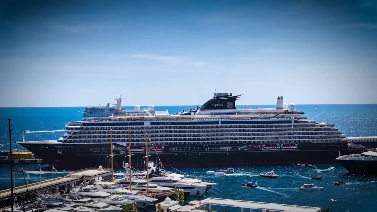 Large Explorer-class cruise ship docked in Monaco harbour with yachts and blue sea