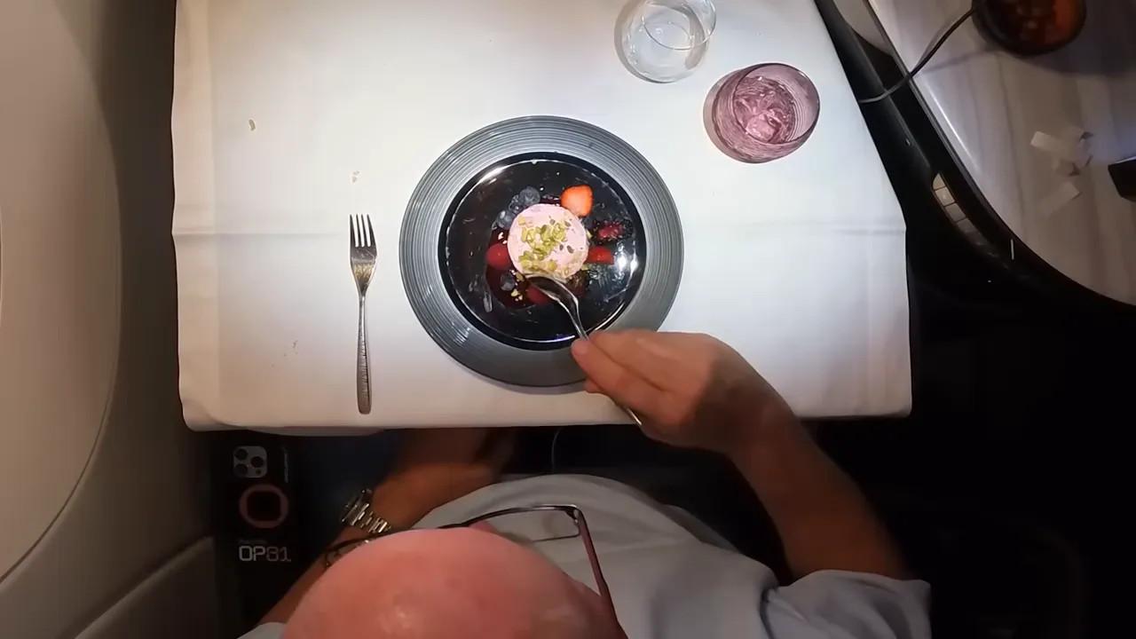 Overhead shot of a plated dessert with berries and a hand using a spoon in business class