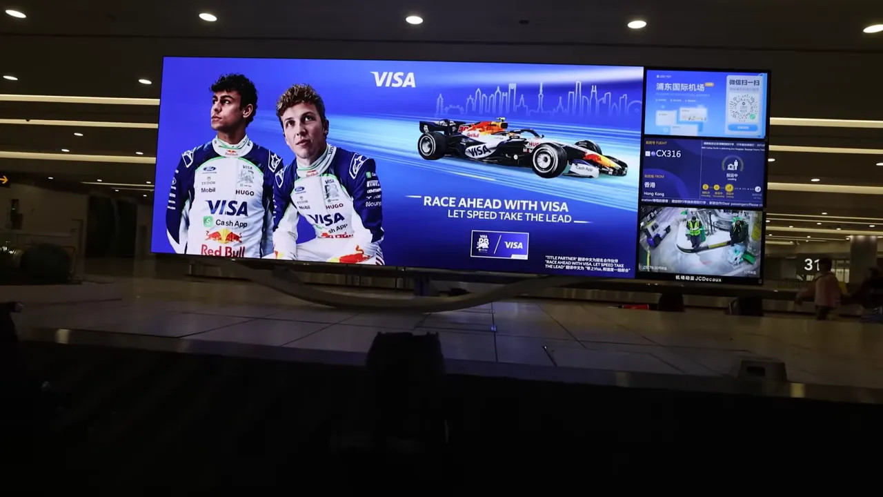 Baggage carousel with a large VISA advertisement on the screen behind it