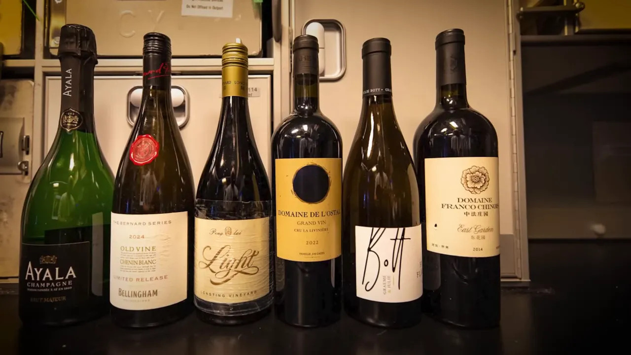 Row of in‑flight wine bottles including Chinese and international labels on a galley surface.