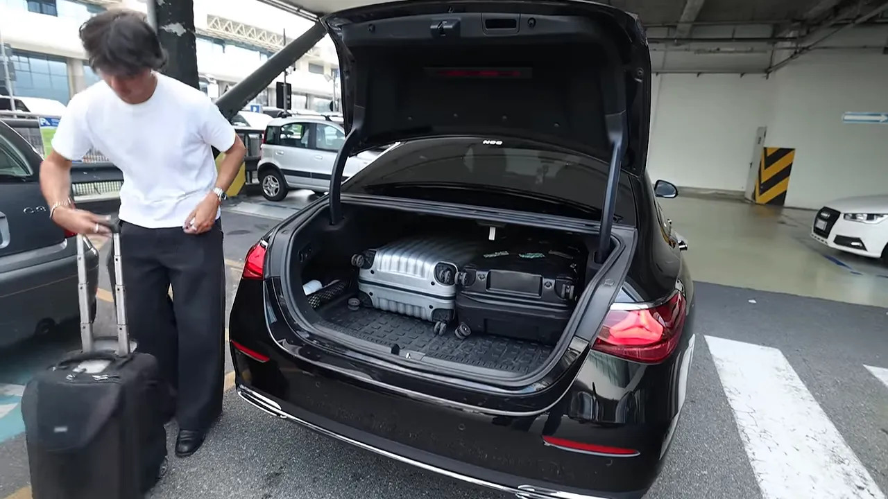 Open boot of a black Mercedes with suitcases inside at an airport pickup area