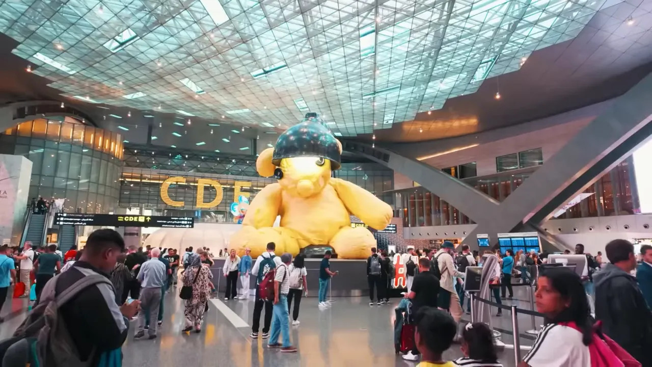travellers around large yellow teddy bear art installation in Hamad International terminal