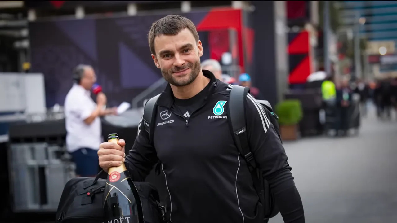 Team member smiling in the paddock while carrying a travel bag and a large champagne bottle.