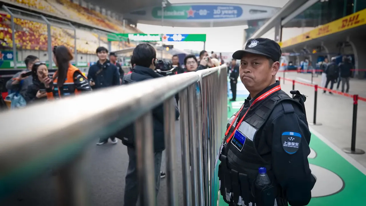 Track security marshal beside prominent metal barrier at pit lane illustrating fencing and access control