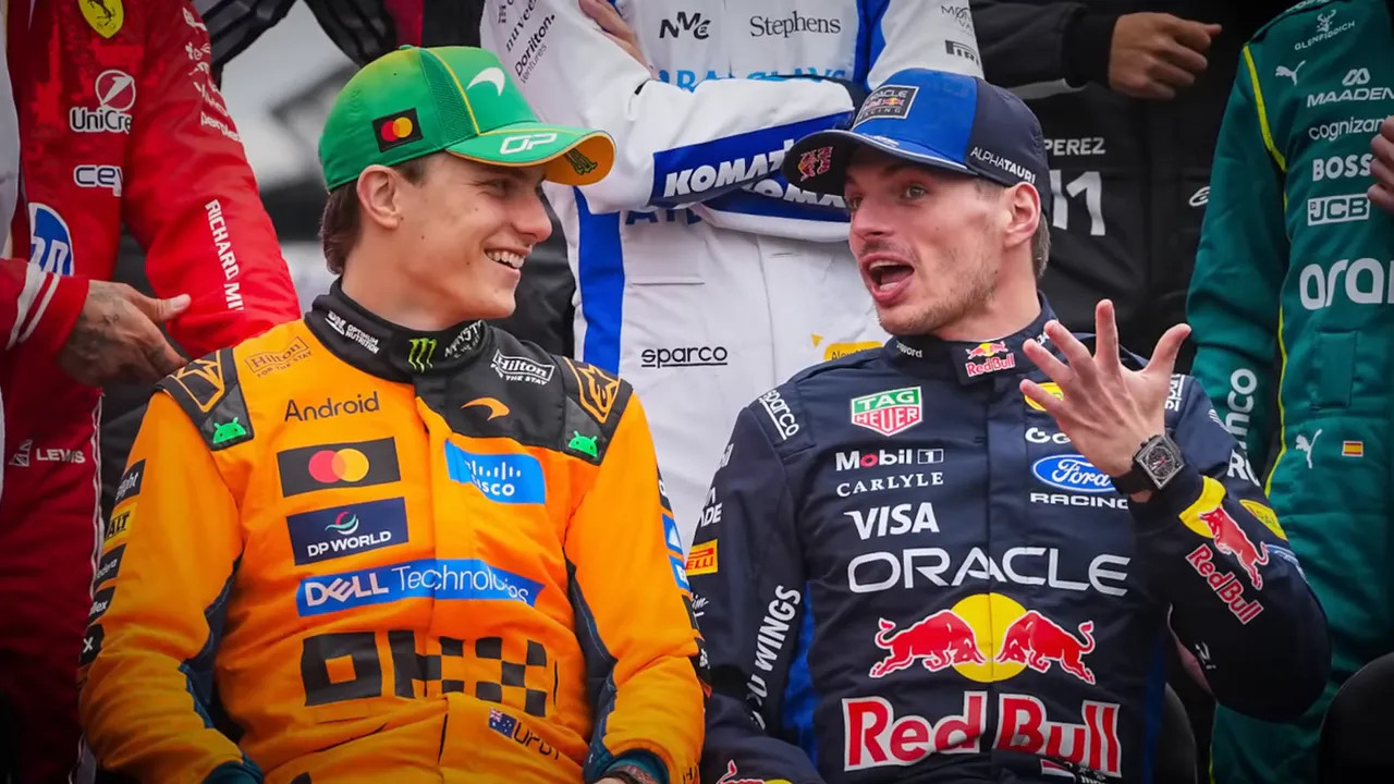 Two Formula 1 drivers talking animatedly during a group shot, with team liveries visible