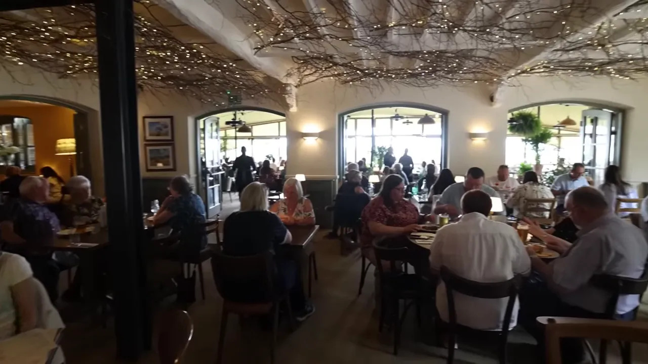 Busy stone dining room with tables full of diners under a textured ceiling and large windows
