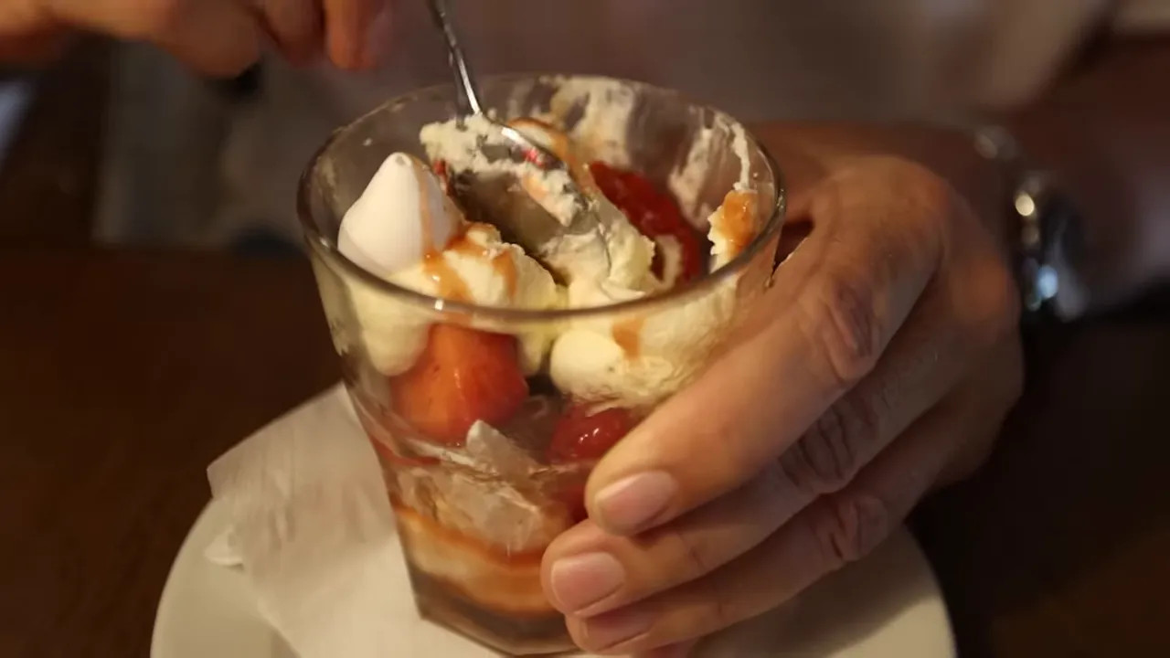 Glass dessert with strawberries cream meringue and sauce held over a white saucer
